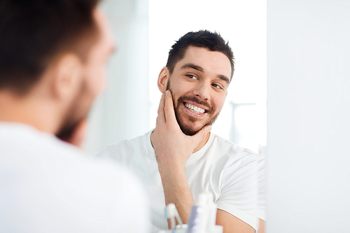 beauty, hygiene and people concept - smiling young man looking to mirror at home bathroom
