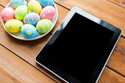 easter, holidays, technology, advertisement and object concept - close up of colored easter eggs on plate and blank tablet pc computer