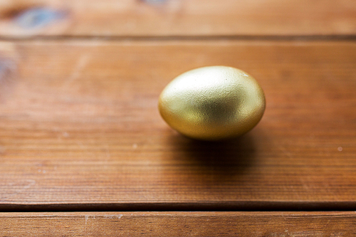 easter, holidays, tradition and object concept - close up of golden easter egg on wood