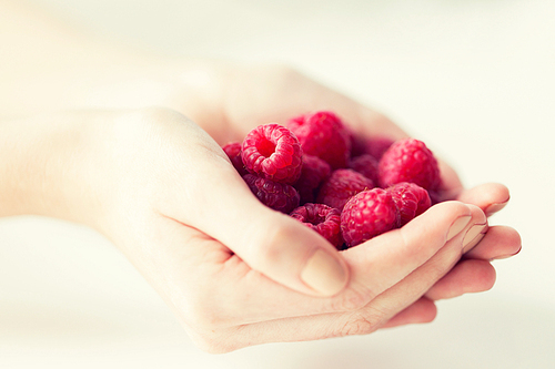 healthy eating, dieting, vegetarian food and people concept - close up of woman hands holding raspberries at home