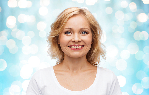 happiness and people concept - smiling woman in blank white t-shirt over blue holidays lights background