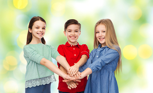 childhood, friendship, summer holidays, friendship and people concept - happy smiling children with hands on top over green lights background