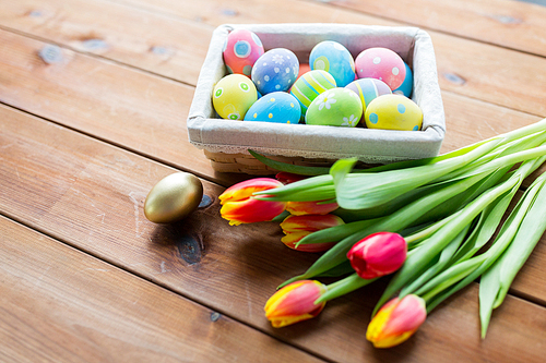 easter, holidays, tradition and object concept - close up of colored easter eggs in basket and tulip flowers