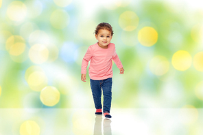 childhood, fashion, clothing and people concept - beautiful little african american baby girl walking over green summer light background