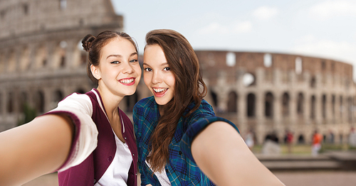 people, travel, tourism and friendship concept - happy smiling pretty teenage girls taking selfie over coliseum in rome background