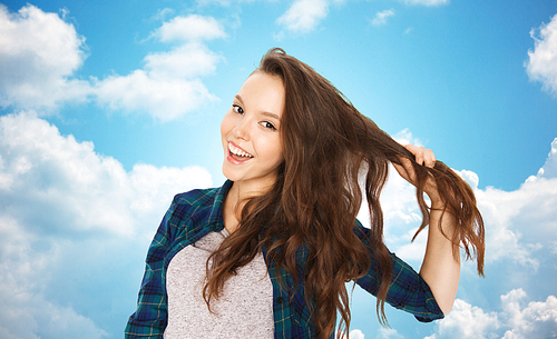 people, hair care, style and teens concept - happy smiling pretty teenage girl holding strand of her hair over blue sky and clouds background