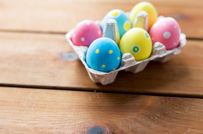 easter, holidays, tradition and object concept - close up of colored easter eggs in egg box or carton wooden surface