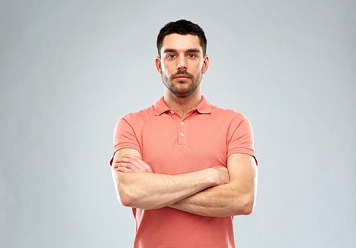 people concept - serious young man in polo t-shirt with crossed arms over gray background