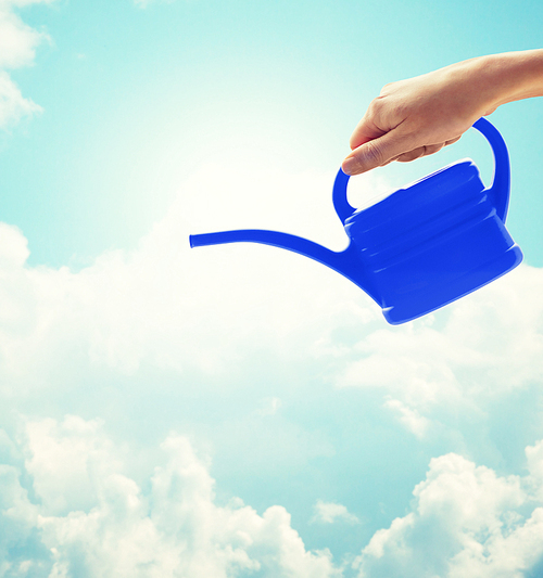 people, gardening and profession concept - close up of woman or gardener hand holding watering can over blue sky with clouds