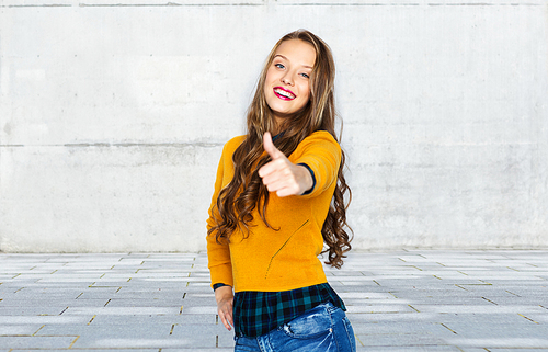 people, gesture, style and fashion concept - happy young woman or teen girl in casual clothes showing thumbs up over urban street background