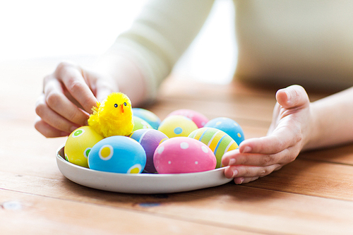 easter, holidays, tradition and people concept - close up of woman hands with colored easter eggs on plate