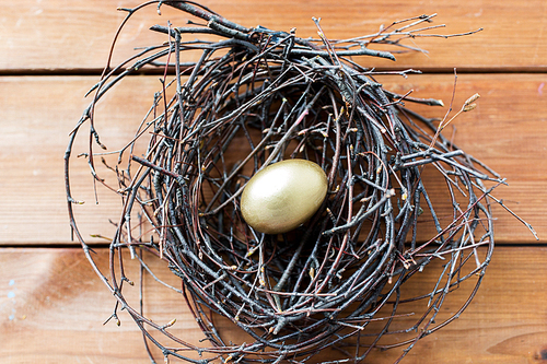 easter, holidays, tradition and object concept - close up of golden easter egg in nest on wooden surface