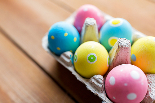 easter, holidays, tradition and object concept - close up of colored easter eggs in egg box or carton wooden surface