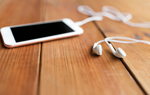 technology, music, gadget and object concept - close up of white smartphone and earphones on wooden surface with copy space