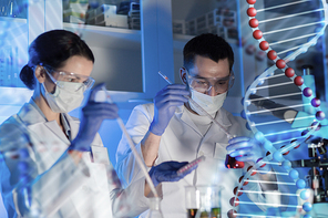 science, chemistry, biology, medicine and people concept - close up of young scientists with pipette and flasks making test or research in clinical laboratory over dna molecule structure