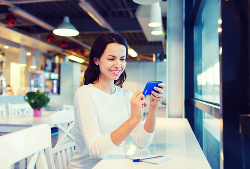 business, people, technology and lifestyle concept - smiling young woman texting message with smartphone at cafe