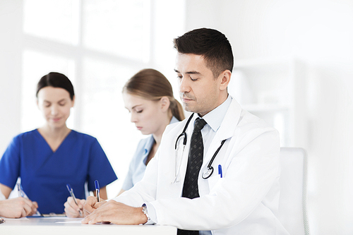 hospital, profession, people and medicine concept - group of happy doctors meeting and taking notes at medical office