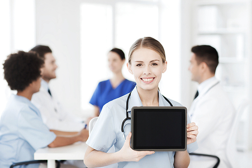 clinic, profession, people and medicine concept - happy female doctor showing tablet pc computer blank screen over group of medics meeting at hospital