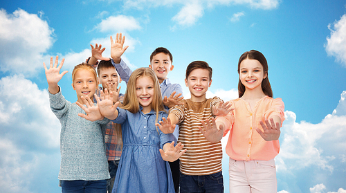 childhood, friendship, gesture and people concept - happy smiling children waving hands over blue sky and clouds background