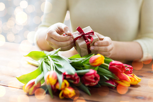people, holidays and greeting concept - close up of woman holding gift box and tulip flowers