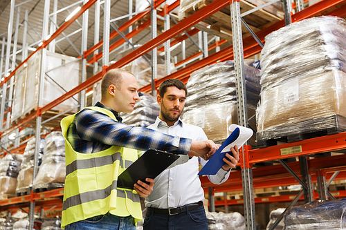 wholesale, logistic, people and export concept - manual worker and businessmen with clipboards at warehouse