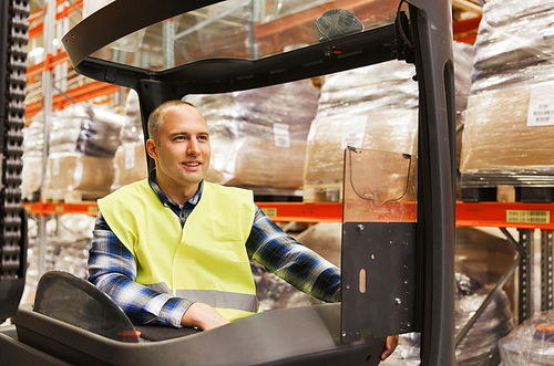 wholesale, logistic, loading, shipment and people concept - smiling man or loader operating forklift loader at warehouse