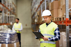 wholesale, logistic, people and export concept - man with clipboard in reflective safety vest at warehouse