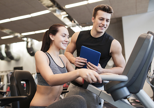 sport, fitness, lifestyle, technology and people concept - happy woman with trainer working out on exercise bike in gym