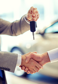 auto business, car sale, deal, gesture and people concept - close up of dealer giving key to new owner and shaking hands in auto show or salon