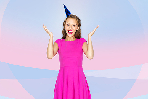 people, holidays, emotion, expression and celebration concept - happy young woman or teen girl in pink dress and party cap over pink violet background