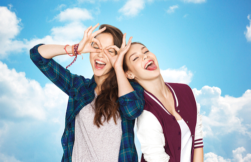 people, friends, teens and friendship concept - happy smiling pretty teenage girls having fun and making faces over blue sky and clouds background