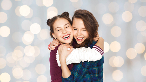 people, friends, teens and friendship concept - happy smiling pretty teenage girls hugging and laughing over holidays lights background