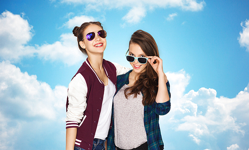 people, friendship, fashion, summer and teens concept - happy smiling pretty teenage girls in sunglasses over blue sky and clouds background