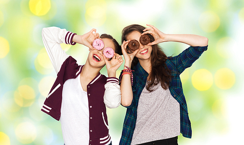 people, friends, teens and friendship concept - happy smiling pretty teenage girls with donuts making faces and having fun over green holidays lights background