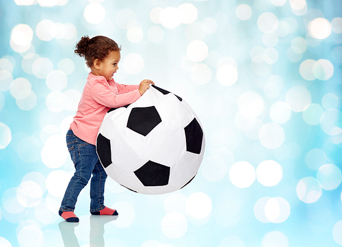 childhood, game, football and people concept - happy african american little baby girl playing with ball over blue holidays lights background