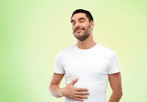 satisfaction, healthy eating and people concept - happy full man touching his tummy over green background