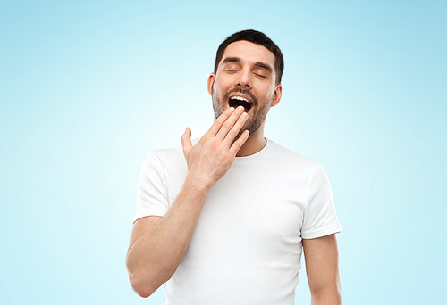 rest, bedtime and people concept - tired sleepy yawning man over blue background