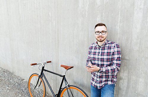 people, style, technology, leisure and lifestyle - happy young hipster man in earphones with smartphone and fixed gear bike listening to music on city street