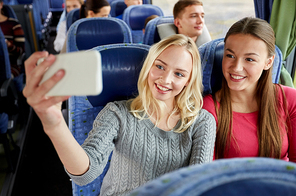 transport, tourism, road trip and people concept - happy young women or friends in travel bus taking selfie by smartphone