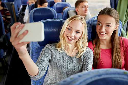 transport, tourism, road trip and people concept - happy young women or friends in travel bus taking selfie by smartphone