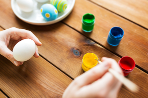 easter, holidays, tradition and people concept - close up of woman hands coloring easter eggs with colors and brush