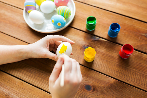 easter, holidays, tradition and people concept - close up of woman hands coloring easter eggs with colors and brush