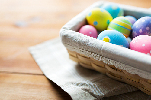 easter, holidays, tradition and object concept - close up of colored easter eggs in wicker basket