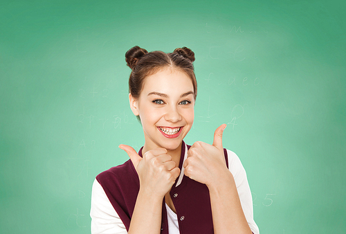 people, gesture, emotions, education and teens concept - happy smiling pretty teenage girl showing thumbs up over green school chalk board background