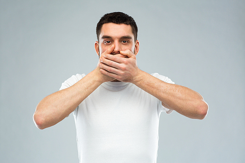 emotion, silence and people concept - man in white t-shirt covering his mouth with hands over gray background