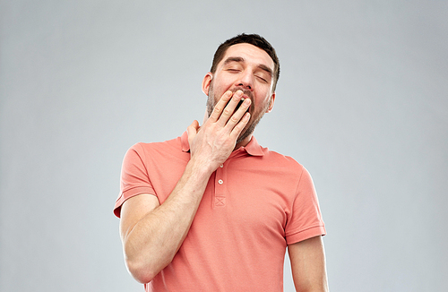 rest, bedtime and people concept - tired yawning man over gray background