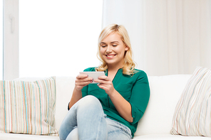 people, technology, communication and leisure concept - happy young woman sitting on sofa with smartphone at home