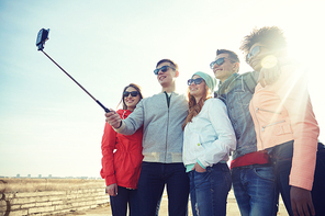 tourism, travel, people, leisure and technology concept - group of smiling teenage friends taking selfie with smartphone and monopod on city street