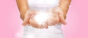 people and magic concept - close up of twinkles or fairy dust on female cupped hands over pink background