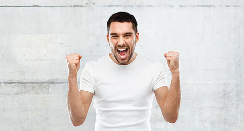 emotion, success, gesture and people concept - young man celebrating victory over gray stone wall background